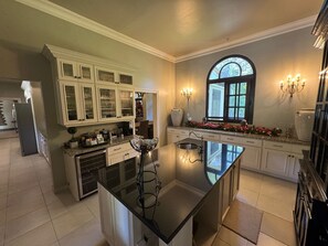 Une cuisine spacieuse dotée d’un grand îlot central, de meubles blancs et d’une fenêtre décorative.