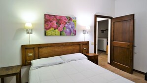Une chambre à coucher avec une tête de lit en bois, un lit recouvert de draps blancs, deux lampes de chevet et un tableau floral accroché au mur.