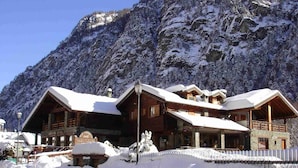 Eine Holzhütte mit mehreren Balkonen und einem mit Schnee bedeckten Dach, vor einer Berglandschaft.