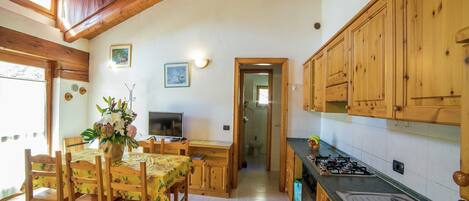 Une cuisine avec des meubles en bois, une table à manger avec des chaises, un téléviseur et une vue sur la salle de bain.