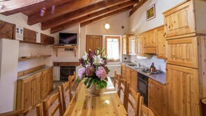 A wooden kitchen with a dining table, chairs, and a TV mounted on a wooden shelf.