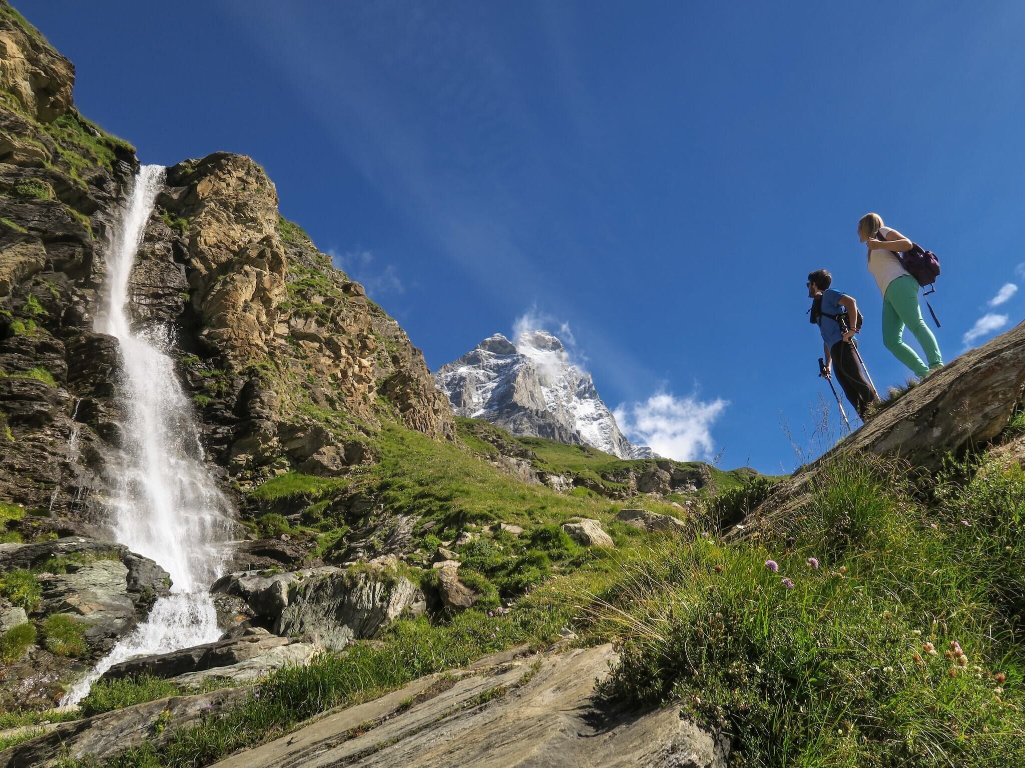 Ein Wasserfall stürzt über eine felsige Klippe, Wanderer stehen auf einem Vorsprung.