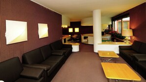 A hotel lobby with a dark patterned wall, a reception desk, a bar area, and seating arrangements including sofas and tables.