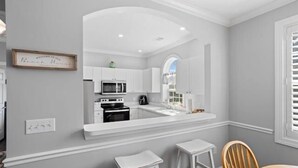 A modern kitchen with white cabinetry, a built-in microwave, and a large island with stools.