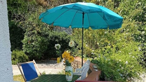 Une terrasse extérieure avec une table et des chaises, un parasol bleu et un vase rempli de fleurs.