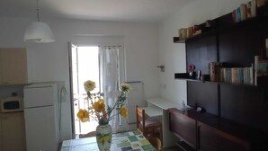 Une petite pièce bien éclairée, avec une table à manger, des chaises, une bibliothèque et un réfrigérateur.