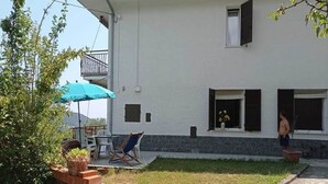 Une maison à deux étages avec un balcon, un petit jardin et un patio aménagé avec du mobilier d’extérieur.