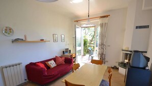 A compact living space with a red sofa, a wooden dining table, and a kitchenette. - Escape Near Cinque Terre (Moneglia)