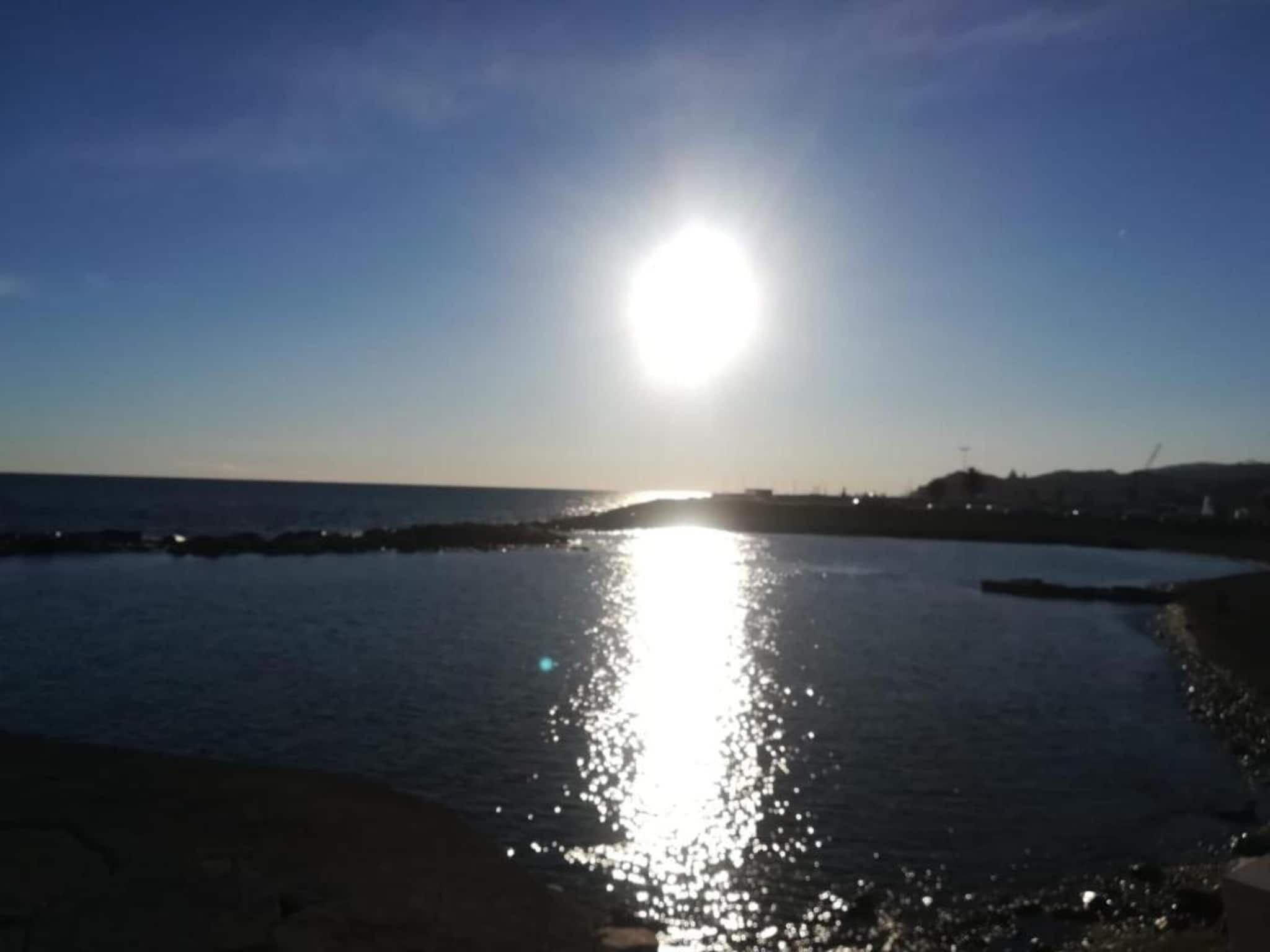 Une étendue d’eau qui reflète le soleil, sous un ciel dégagé, avec une côte lointaine à l’horizon.