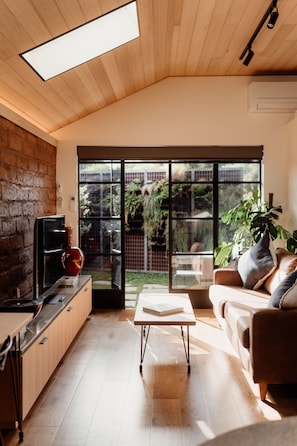 A modern kitchen with a wooden ceiling, a large window, and a sliding glass door leading to a garden. - Great 50 meter square architectural fitout with a cosy modern vibe to relax in  (Surf Beach)