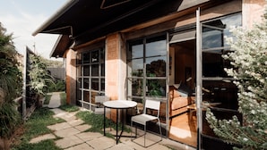 A modern house with large windows, a patio with a table and chairs, and a garden area. - Great 50 meter square architectural fitout with a cosy modern vibe to relax in  (Surf Beach)