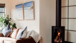 A cozy living room with a sofa, a round table, and a black wood-burning stove. - Great 50 meter square architectural fitout with a cosy modern vibe to relax in  (Surf Beach)
