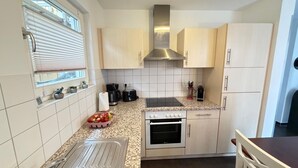 A compact kitchen with white cabinets, a stainless steel range hood, a built-in oven, and a countertop with a coffee maker and toaster.