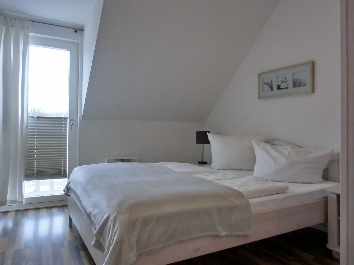 Un dormitorio con cama, ventana con persianas, radiador y un cuadro en la pared.