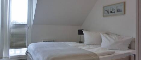 Un dormitorio con cama, ventana con persianas, radiador y un cuadro en la pared.