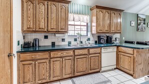 Una cocina con armarios de madera, salpicadero de azulejos, una ventana con cortinas y una cafetera.