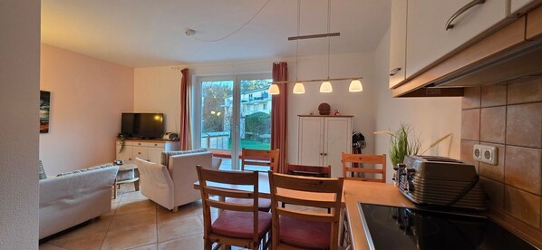 A modern living room with a sofa, chairs, a dining table, and a kitchen area with a stove and cabinets.