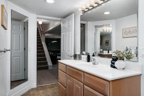 A modern bathroom with a large mirror, white vanity, and a shower area.
