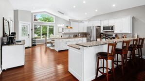 Una cocina moderna con armarios blancos, una isla grande con taburetes y vistas al exterior.