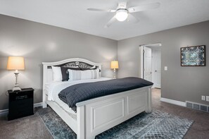 A bedroom with a white bed, two bedside lamps, a ceiling fan, and a patterned rug.
