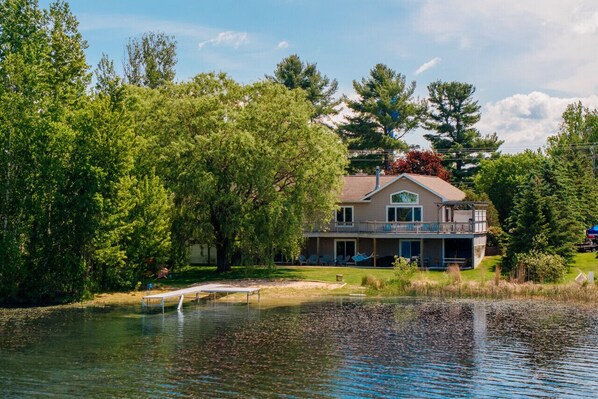 A two-story house with a balcony, surrounded by trees and a body of water.