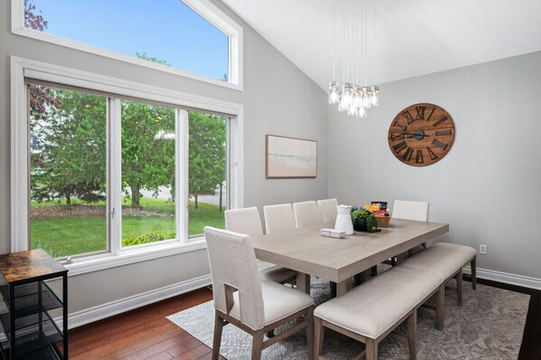 A dining area with a large window, a wooden clock, and a chandelier.