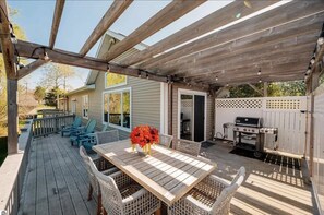 A wooden deck with a table and chairs, a grill, and a covered area with string lights.