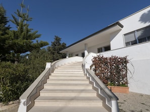 Un escalier en béton mène à un bâtiment blanc doté d’un porche abrité.
