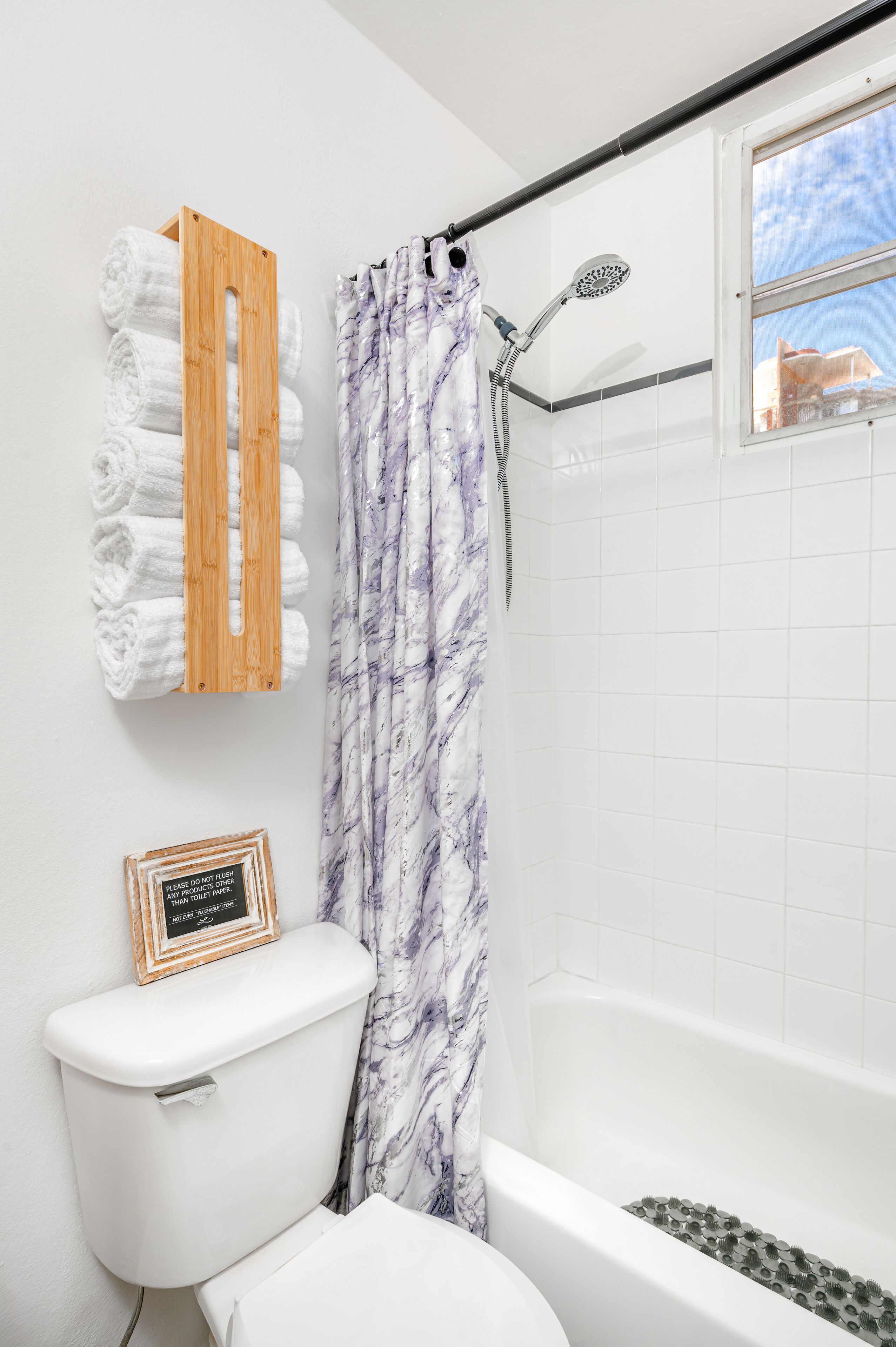 A bathroom with a toilet, a shower with a marble curtain, and a towel rack with neatly folded towels.