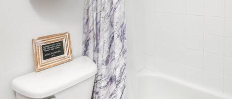 A bathroom with a toilet, a shower with a marble curtain, and a towel rack with neatly folded towels.