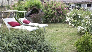 Un jardín con dos sillones blancos, un muro de piedra y diversas plantas en flor.