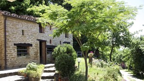 Edificio de piedra con un jardín delantero, que incluye escalones que conducen a la entrada, plantas en macetas y un sendero.
