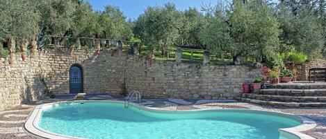 Une piscine avec un mur en pierre et des marches menant à l’eau, le tout entouré de verdure.