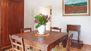 Ein Esszimmer mit Holztisch, Stühlen, einer weißen Vase mit Blumen, einem Bild von einem Feld und einem Holzschrank.