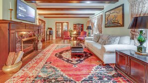 A spacious living room with a large TV, a fireplace, a patterned rug, and a white sofa. - Spacious Jamestown Home Near Nat'l Comedy Center! (Jamestown)