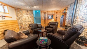 Acogedor interior de cabaña de madera con sofás de cuero, una mesita y una pared de piedra.