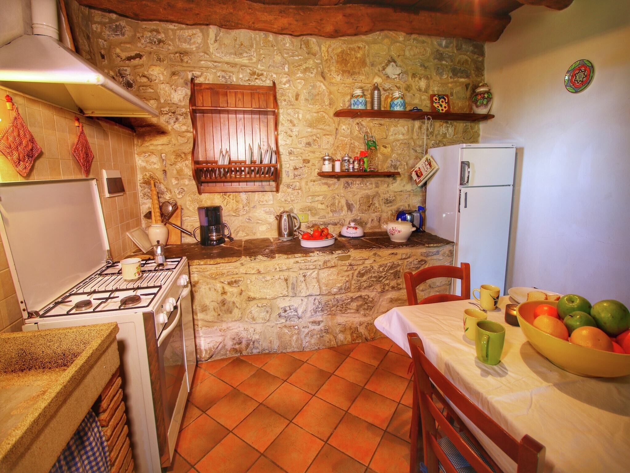 A rustic kitchen with a stone wall, wooden cabinets, and a tiled floor.