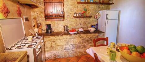 A rustic kitchen with a stone wall, wooden cabinets, and a tiled floor.