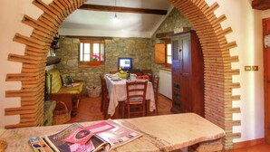 A dining area with a stone wall, a wooden table set for two, and a television on the wall. - Charming Tuscan Farmhouse (Ortignano)