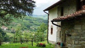 A rustic stone building with a tiled roof, surrounded by lush greenery and a view of a valley with scattered houses. - Charming Tuscan Farmhouse (Ortignano)