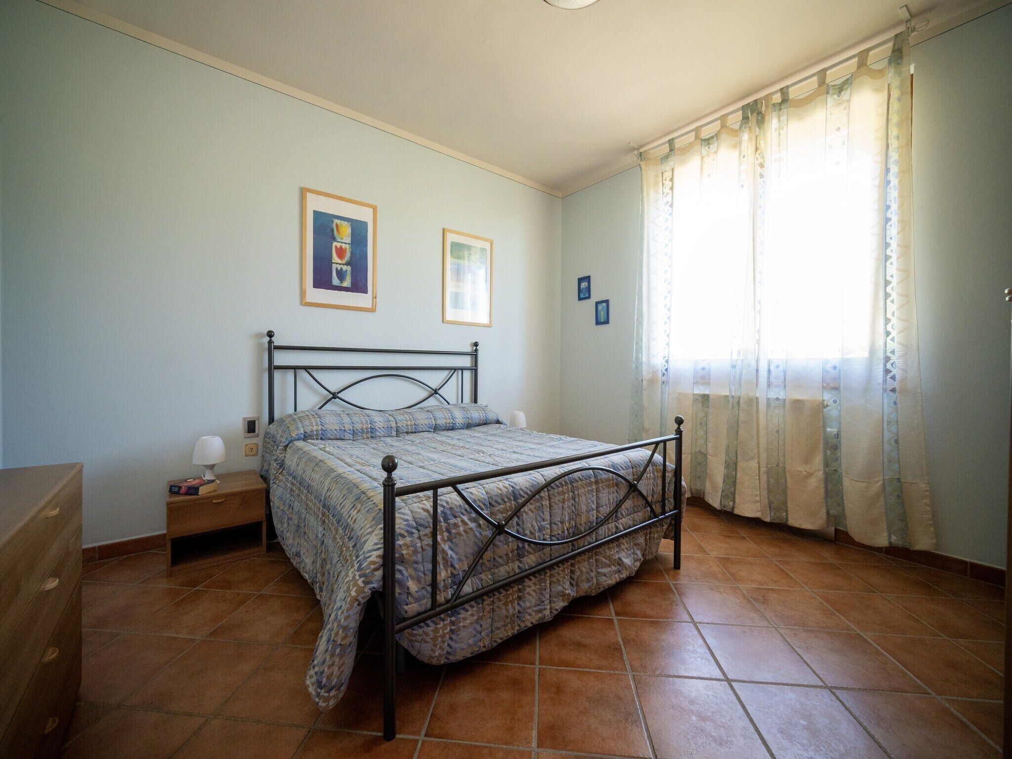 A bedroom with a bed, a nightstand, a dresser, and a window with curtains.