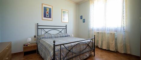 A bedroom with a bed, a nightstand, a dresser, and a window with curtains.
