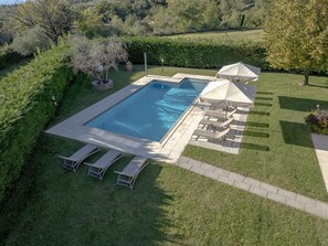 Ein rechteckiger Pool mit bepflasterter Liegefläche, umgeben von einem gepflegten Rasen und einem Heckenstreifen.