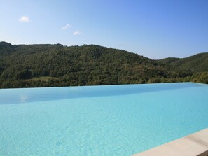 Una piscina infinita de color azul cristalino con vistas a un paisaje montañoso cubierto de bosque.