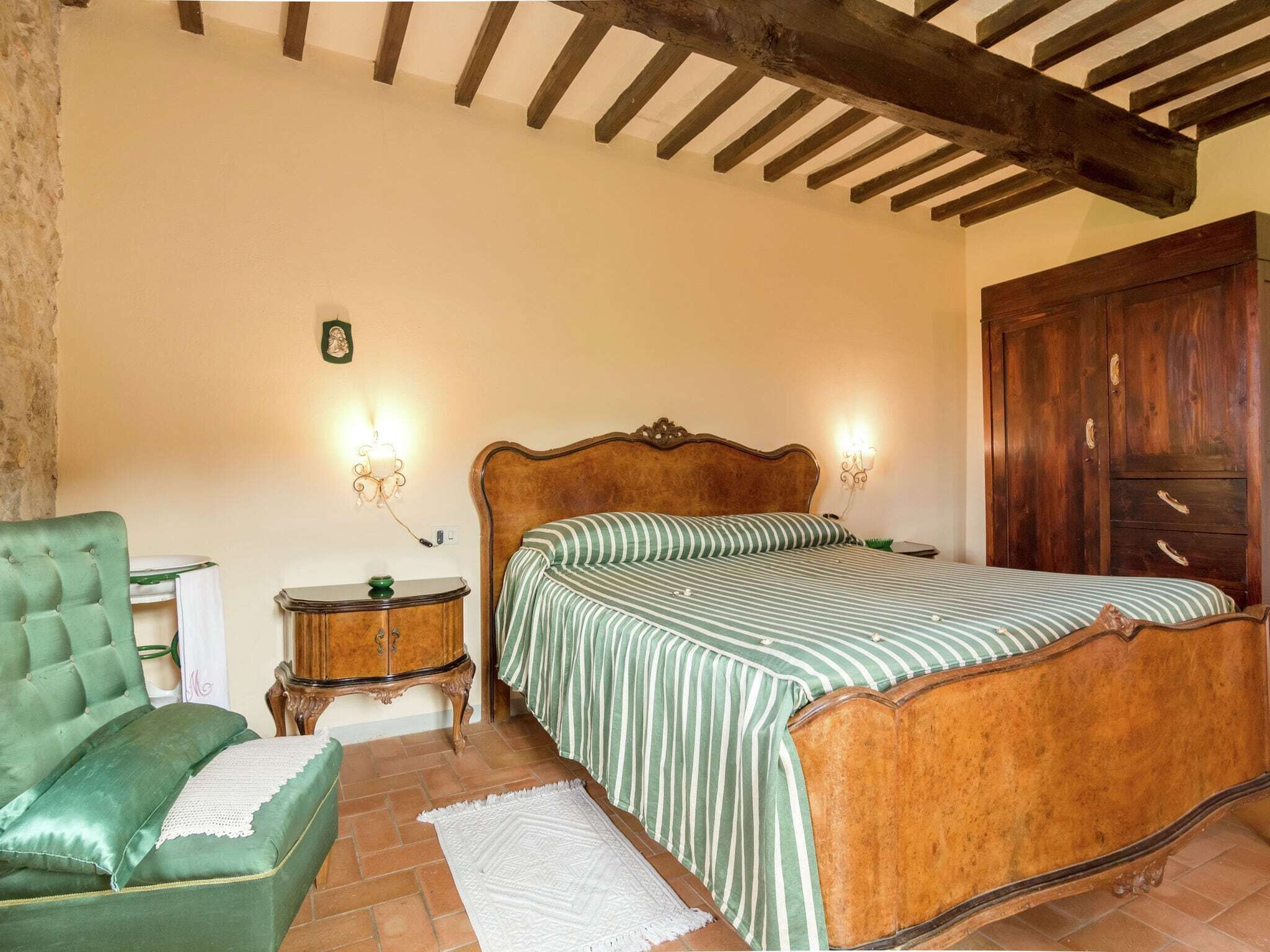 A bedroom with a wooden bed, a green armchair, a nightstand, and a wardrobe.
