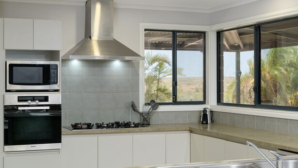 A modern kitchen with a microwave, oven, and gas stove. There is a window with a view of palm trees and a desert landscape. - 79 Nimitz Street - Pool and Pet Friendly (Exmouth)