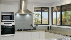 Eine moderne Küche mit Mikrowelle, Backofen und Gasherd. Ein Fenster bietet Blick auf Palmen und eine Wüstenlandschaft.