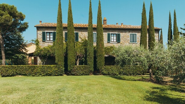 A stone building with a tiled roof, green shutters, and tall cypress trees in the foreground. - Belvilla by OYO Pino (Cortona)