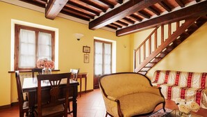 A dining area with a wooden table and chairs, a sofa with patterned cushions, and a staircase with wooden railings. - Belvilla by OYO Pino (Cortona)