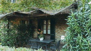 A rustic stone building with a thatched roof, a table with chairs, and lush greenery. - holiday home in Cortona (Cortona)